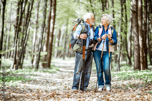 Beautiful senior couple hiking with backpacks and trekking sticks in the forest. Concept of active lifestyle on retirement © rh2010