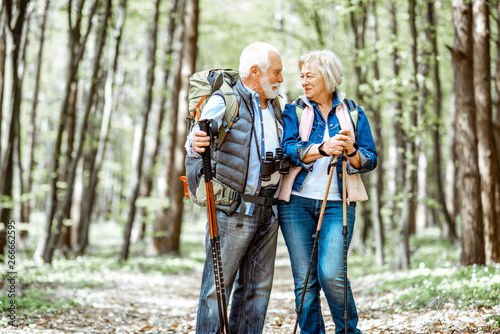 Beautiful senior couple hiking with backpacks and trekking sticks in the forest. Concept of active lifestyle on retirement