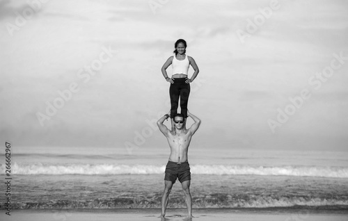 outdoors lifestyle portrait young attractive and concentrated couple of yoga acrobats practicing acroyoga balance and meditation exercise on beautiful beach