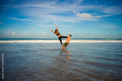 outdoors lifestyle portrait young attractive and concentrated couple of yoga acrobats practicing acroyoga balance and meditation exercise on beautiful beach
