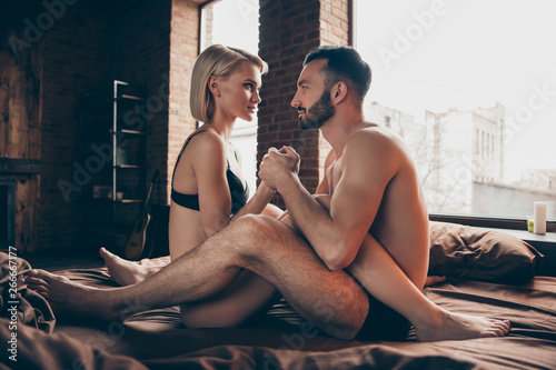 Best night evening alone at hotel. Side profile photo of charming attractive blonde bob haired busty lady hugging embrace hold hand legs body nude handsome bearded tender careful guy sheets linen
