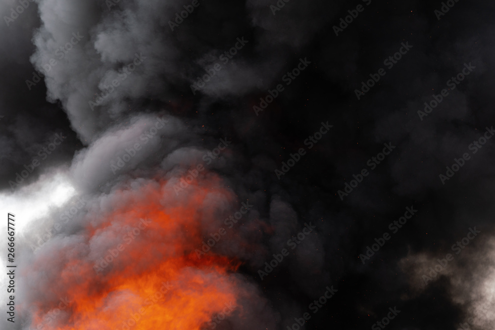 Dangerous flames of strong red fire and motion clouds of black smoke covered sky. Defocus, motion blur from fire and high temperature from flames. Atmospheric and smoke dispersion.