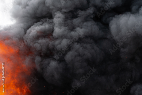 Dangerous flames of red fire and motion clouds of black smoke covered sky. Defocus, motion blur from strong fire and high temperature from flames. Atmospheric and smoke dispersion.