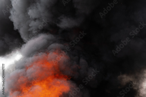Dangerous flames of strong red fire and motion clouds of black smoke covered sky. Defocus  motion blur from fire and high temperature from flames. Atmospheric and smoke dispersion.