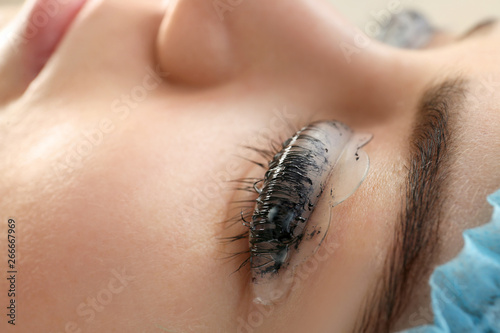 Young woman undergoing procedure of eyelashes dyeing and lamination in beauty salon, closeup photo