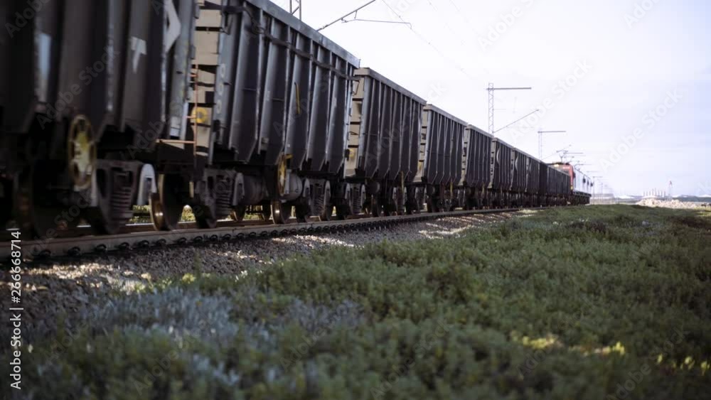 A long logistics train moves iron ore in carriages along railway tracks that pass the camera into the distance. A long logistics train moves iron ore in carriages along railway tracks that pass the camera into the distance.
