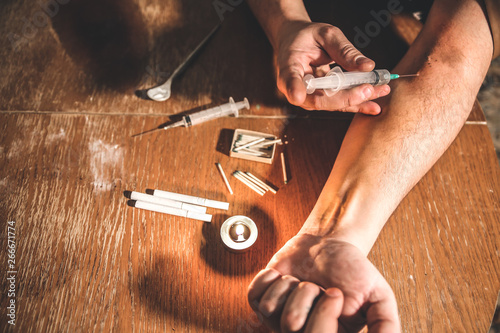 Man shooting heroin with needle syringe. Drugs addict. Candle burning with matches and cigarettes. Dangerous habit. Unhealthy life concept. photo