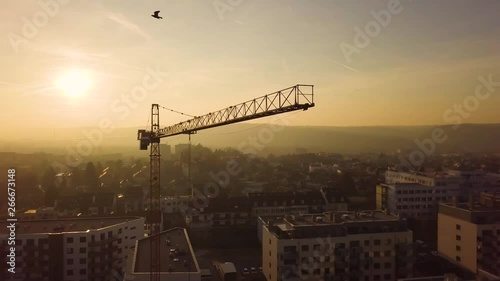 Aerial drone view of construction site crane over city at sunset with mountains in the background. photo