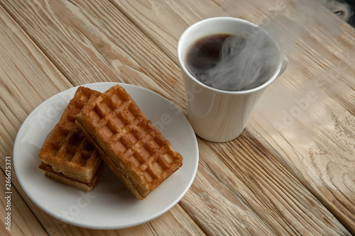 Hot coffee on a wooden stand with waffle, top view