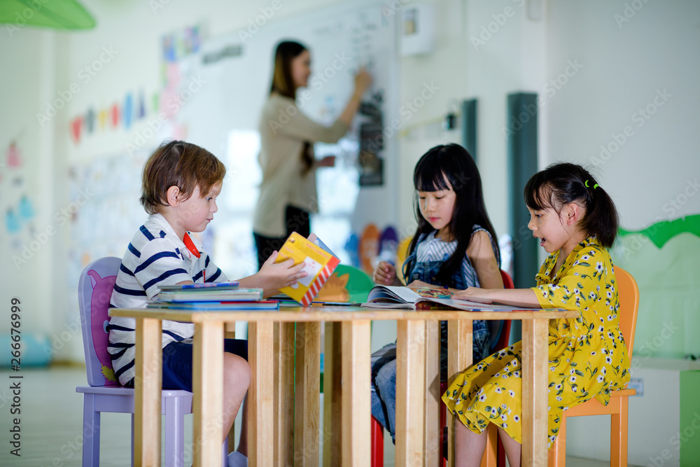 Obraz premium group of international kids in preschool enjoy reading books with teacher watching in background