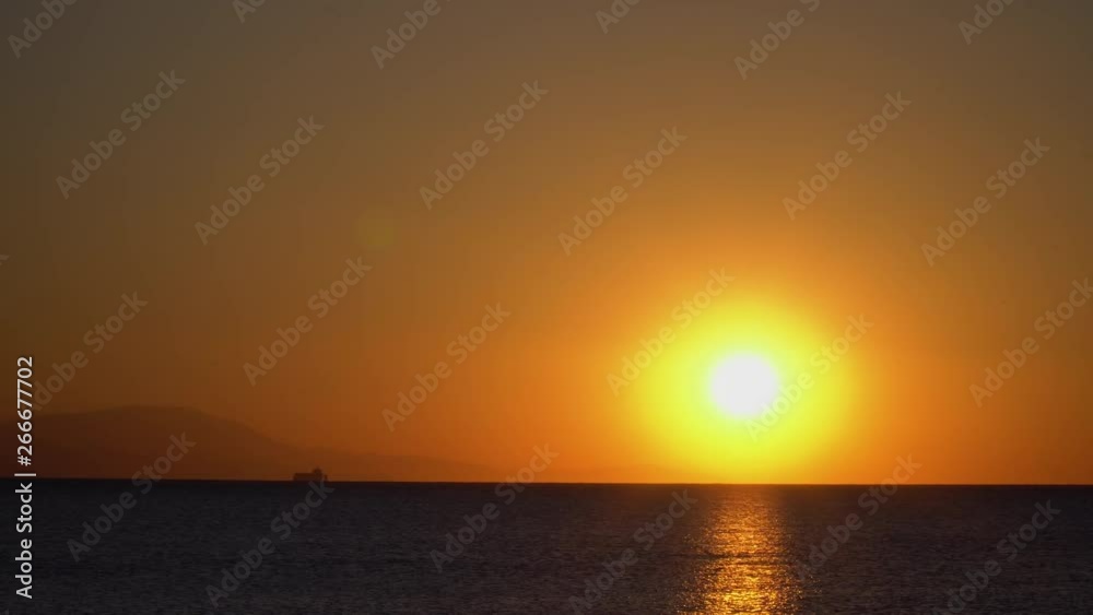 Beautiful and calm static shot of a sunrise with boat and mountains on horizon. Sun reflecting on ocean. Beautiful and calm static shot of a sunrise with boat and mountains on horizon. Sun reflecting on ocean.