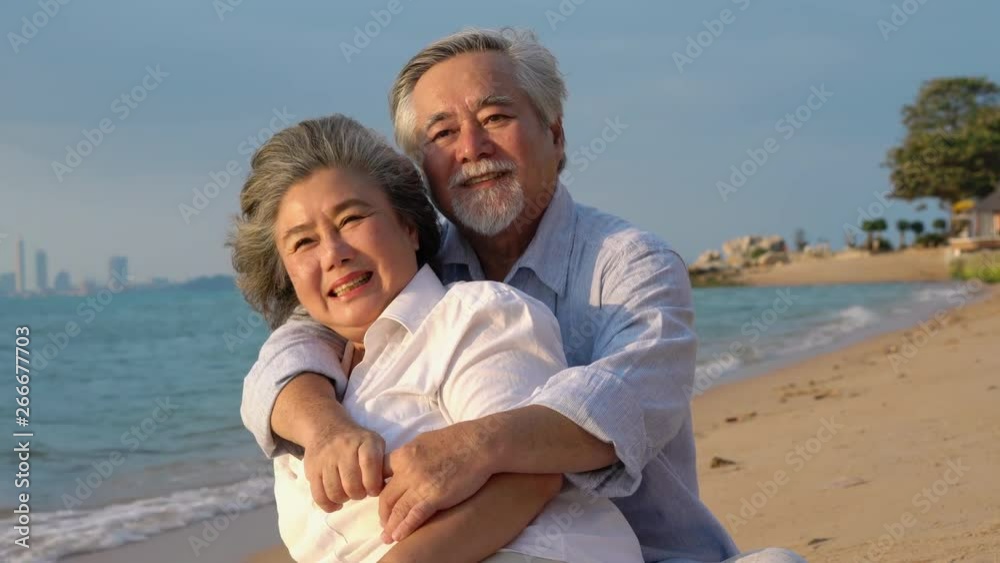 Asian couple senior sitting and relax summer on the beach together. Concept of happy family, post retirement, anniversary married, mental health and summer travel.