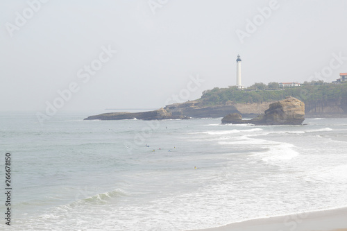 View of a sandy beach and white lighthouse in Biarritz, France.