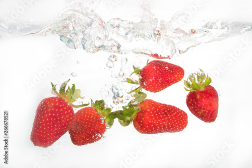 Strawberries splashing in to water on the white