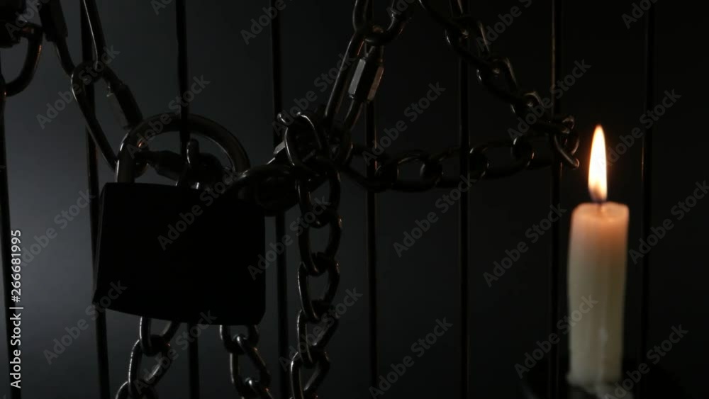 Metal chain, burning candle and padlock on metal fencing on black background Metal chain, burning candle and padlock on metal fencing on black background