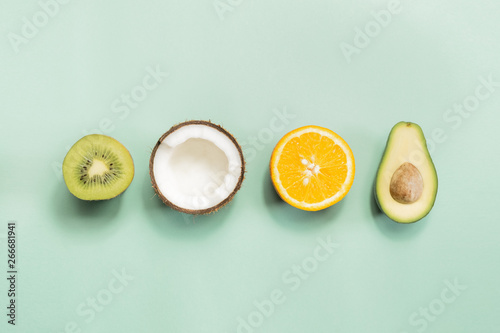 Slika na platnu Kiwi fruit, coconut, orange and avocado on green background