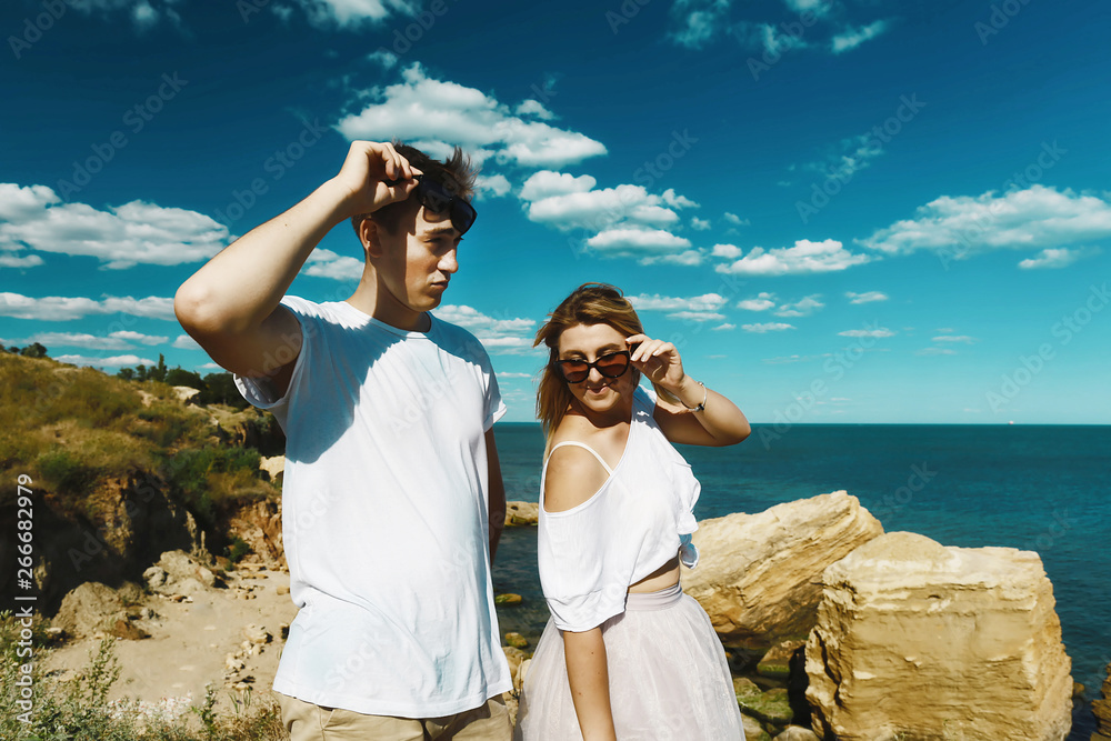 Young man piggybacking his happy girlfriend with raised hand in glasses on the rock in the sea near the beach with big cliffs, Black Sea, Odessa, Ukraine, place for text set