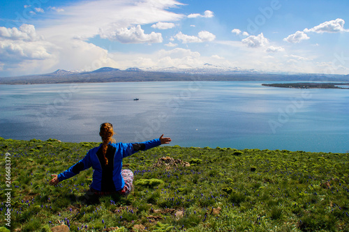 Lake Sevan is the largest body of water in Armenia and in the Caucasus region. Blue expanses of water, mountains, a meadow with flowers and a tourist girl.
