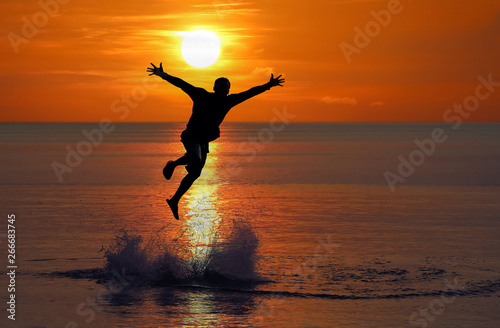 Man jumped up from the sea near the beach at sunset