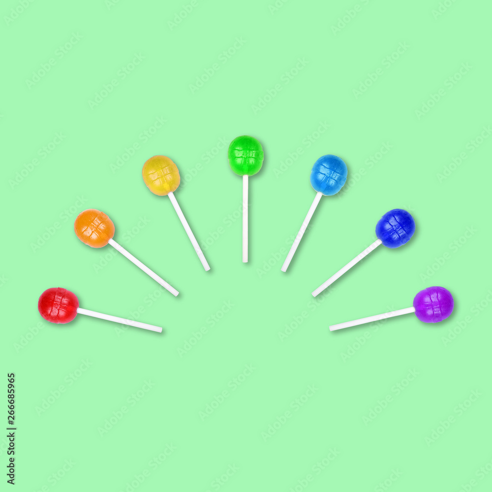 Set of colorful lollipops grouped in a half circle isolated on green background. Candy on a stick. Food background. Flat lay. Set of colorful lollipops grouped in a half circle isolated on green background. Candy on a stick. Food background. Flat lay.