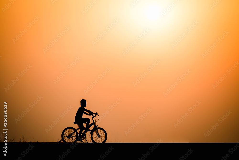 Silhouette boy cycling on sunset background