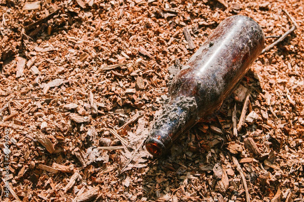 dirty empty bottle left on sawdust in the Park, clogging the environment