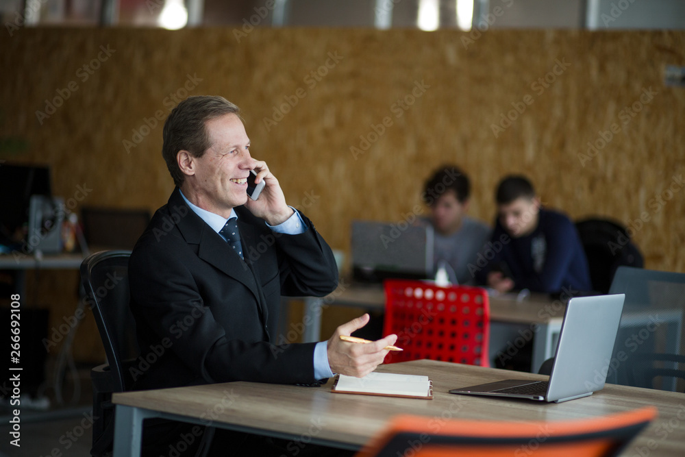 A well dressed businessman is browsing on his mobile phone at the modern office, behind is a window, he is focused and serious. A well dressed businessman is browsing on his mobile phone at the modern office, behind is a window, he is focused and serious.