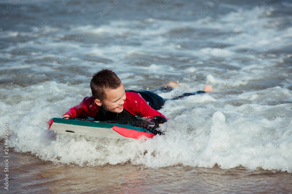 Obraz premium Little Boy Bodyboarding in the Sea