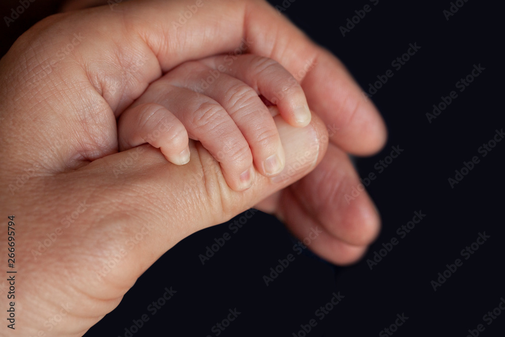 Father holding a newborn baby hand in his. Child hand closeup into parent hands together. Father holding a newborn baby hand in his. Child hand closeup into parent hands together.