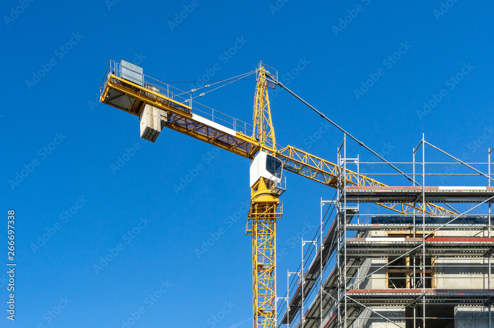 crane on construction site - facade with scaffolding, blue sky without clouds