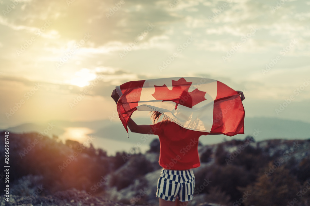 Fototapeta premium Szczęśliwe dziecko nastolatka macha flagą Kanady podczas jazdy o zachodzie słońca