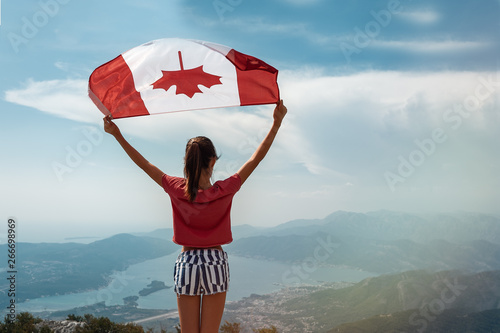 Child girl is waving Canadian flag on top of mountain at sky background