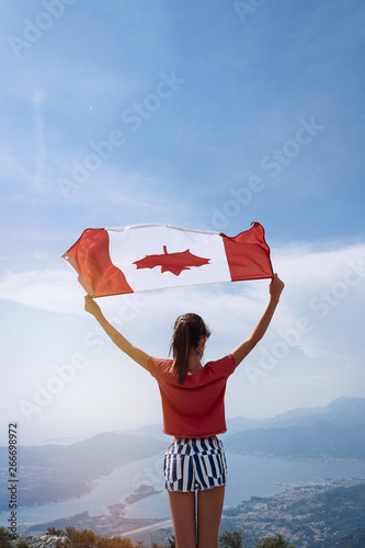 Child girl is waving Canadian flag on top of mountain at sky background