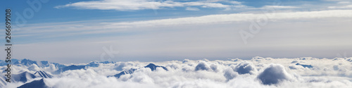 Panoramic airplane view of snowy mountains with sunlit clouds © BSANI