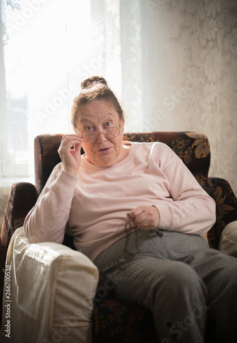 An old woman in glasses sitting in the armchair and knitting. Put the glasses on the nose and looking at something © KONSTANTIN SHISHKIN