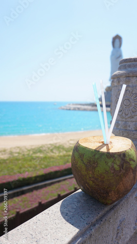 Guanyin of Nanshan, the white statue of the bodhisattva Guanyi near the Nanshan Temple of Sanya, China. In the foreground a coconut cocktail, the sea photo