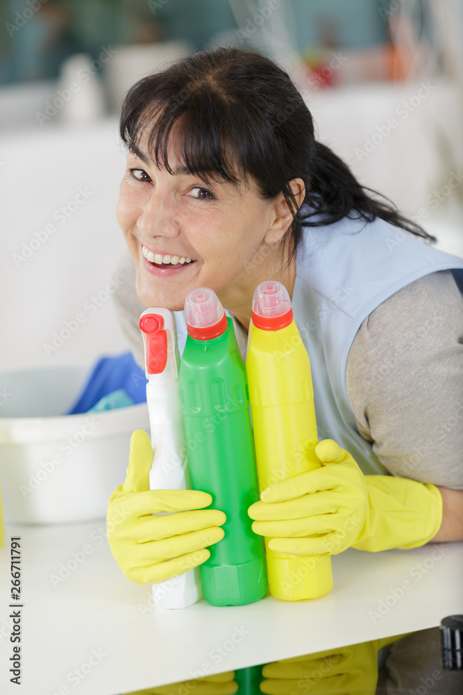 happy mature woman holding spray detergent happy mature woman holding spray detergent