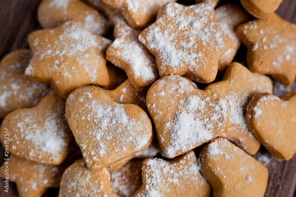 Homemade cookies in the shape of a heart and stars with powdered sugar on a board on a brown wood background, closeup Homemade cookies in the shape of a heart and stars with powdered sugar on a board on a brown wood background, closeup