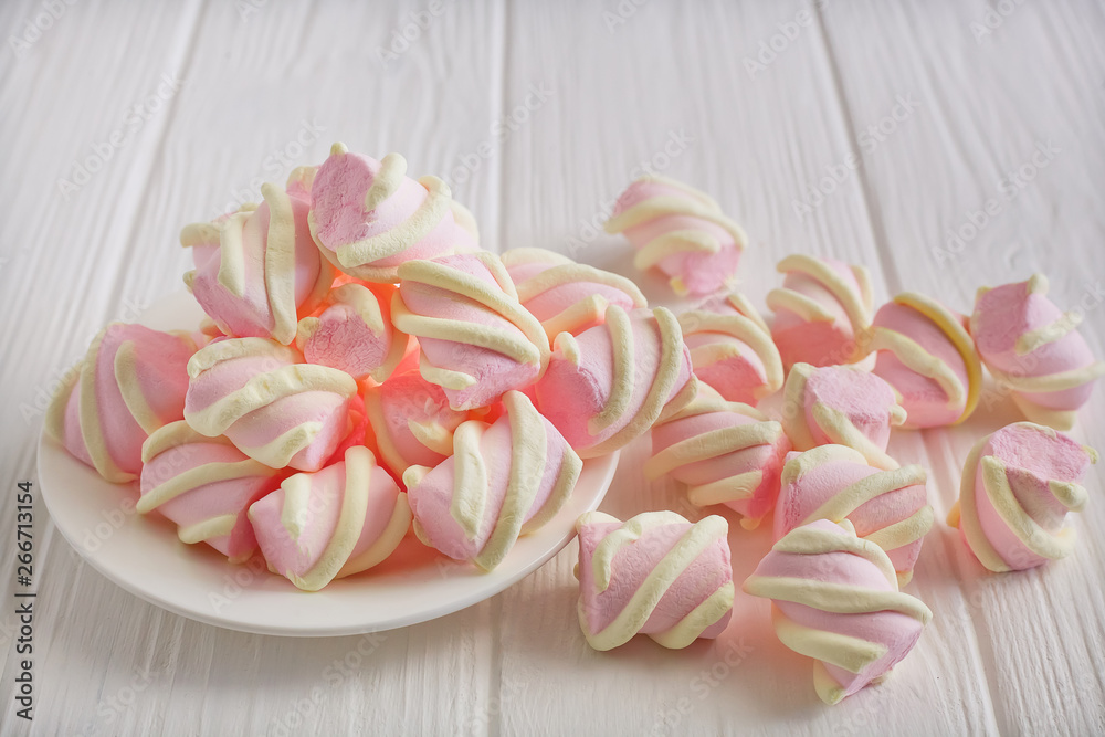 pastel marshmallow flowers on a white saucer on a white wooden table, piled on the table pastel marshmallow flowers on a white saucer on a white wooden table, piled on the table
