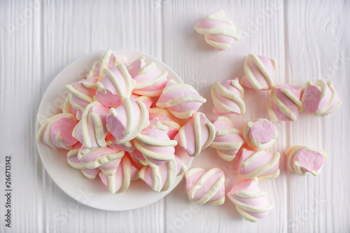 pastel marshmallow flowers on a white saucer on a white wooden table, piled on the table, top view