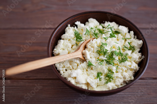 wooden spoon in a bowl with cottage cheese and dill on a brown wooden table background