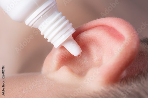 Medical pipette with a drop of medication over the patient's ear
