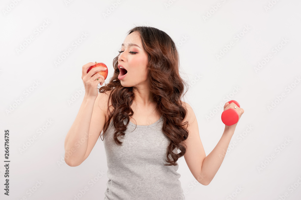 Young fitness model woman athlete in sportswear with red dumbbell and green apple. Healthy life bodybuilding lifestyle concept image, copy space. White empty background for text. Young fitness model woman athlete in sportswear with red dumbbell and green apple. Healthy life bodybuilding lifestyle concept image, copy space. White empty background for text.