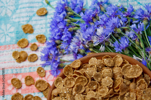 Sugarcorn flakes in a ceramic bowl closeup top view. light breakfast scattered on the table with blue flowers closeup. food fast cooking. healthy food, diet photo