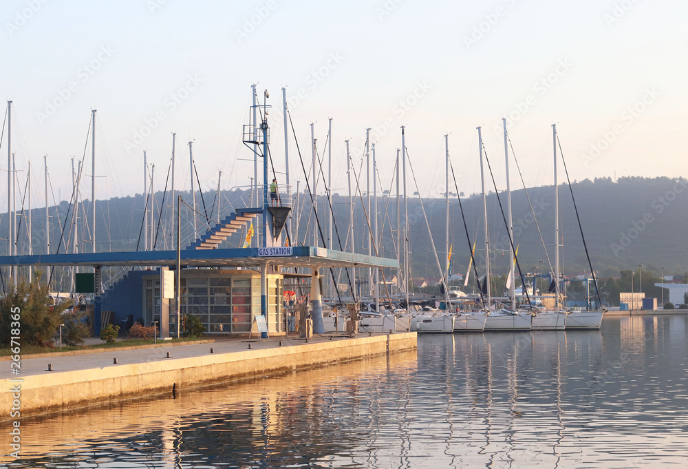 Gas station in the Mediterranean marina on the background of sailing yachts in the rays of sunset. Refueling boats and fishing boats. Infrastructure of the Adriatic port. Saturday charter conditions