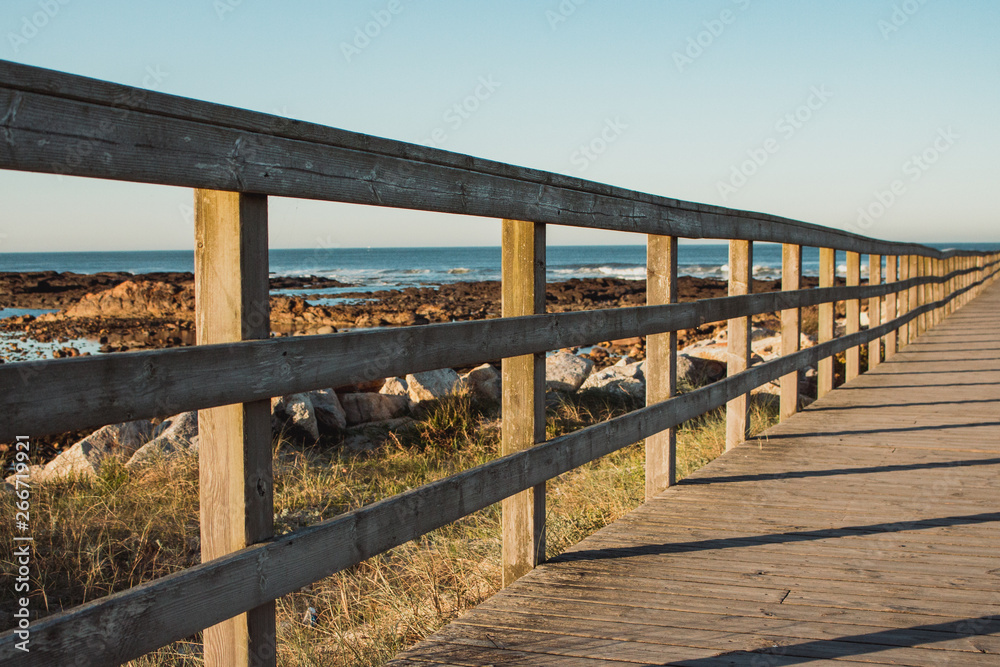 Wooden path with fence to the beach. Walkway on seashore in the morning. Travel and walk concept. Camino de Santiago landscape. Atlantic Ocean coast in Portugal. Wooden pier in perspective. 