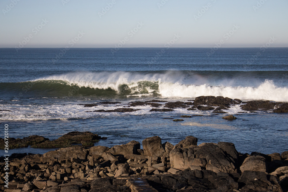 Waves crashing on rocks on Atlantic Ocean beach. Scenic seascape. Beautiful surf at seaside. Splashing waves with foam. Travel and vacation on shore. Rocky coastline. Nature power.