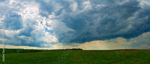 Fototapeta Naklejka Na Ścianę i Meble -  Through the pre-storm clouds make their way to the green field rare rays of the sun