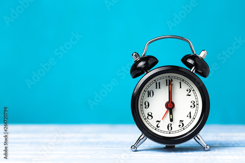 Retro black alarm clock on blue background with copy space. Alarm at 7 clock hand at 6