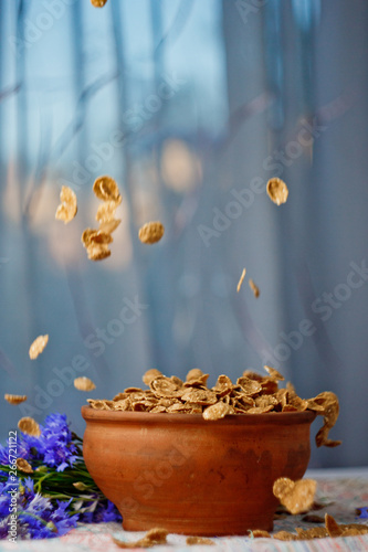 falling sugar cornflakes in a ceramic bowl close-up top view. light breakfast scattered on the table with blue flowers close-up against the window. food fast cooking. healthy food, diet. Vertical
